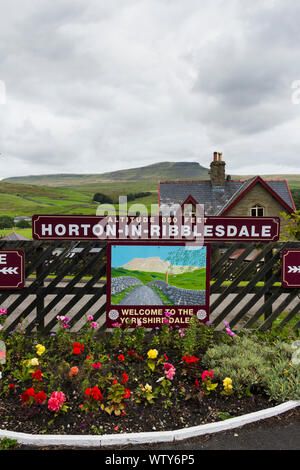 Blumenbeet und Station auf dem Bahnhof in Horton-in-Ribblesdale, North Yorkshire Übersehen von entfernten Pen-Y-Gent. Stockfoto