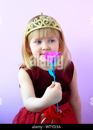 Kleine Mädchen in der Krone riechende Blume. Kleine Prinzessin mit rosa Blume. Nettes Mädchen mit Krone auf dem Kopf mit rosa Rose. Kind im schönen Kleid smil Stockfoto