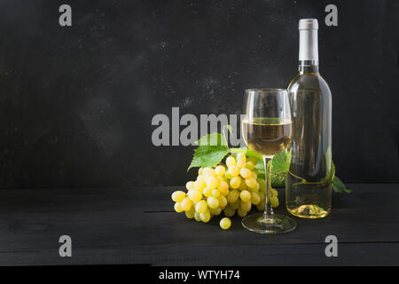 Flasche Weißwein mit Weinglas, reife Trauben auf schwarzer Holztisch. Kopieren Sie Platz. Stockfoto