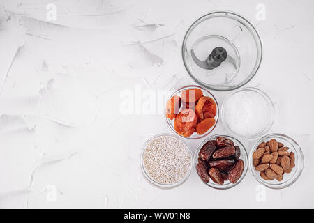 Die Zutaten für eine gesunde Bio Energie Kugeln sind Aprikosen, Kokos Späne, Mandeln, Termine, Sesam und Mixer auf hellem Hintergrund getrocknet Stockfoto