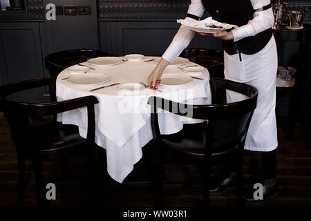 Kellnerin serviert leeres Geschirr, Tisch einstellen. Kellnerin setzt eine Gabel. Stockfoto