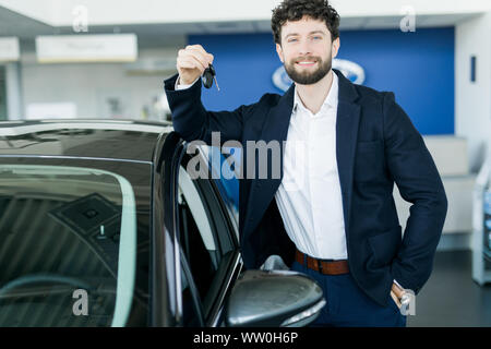 Glückliche Käufer holding Schlüssel in der Nähe des Auto vor der modernen avtosalon Gebäude Stockfoto