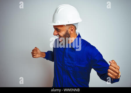 Hübscher indischer Arbeitnehmer Mann einheitliche und Helm tragen über isoliert weißer Hintergrund sehr glücklich und aufgeregt, Sieger Geste mit erhobenen Armen, SMI Stockfoto