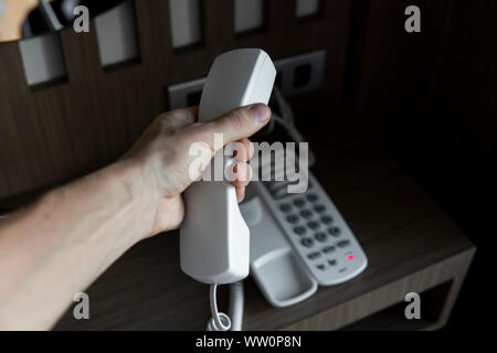 Mans hand Hörer des Weißen vintage Telefon mit grauen battoms auf einem braunen Tisch im Hotel. Stockfoto