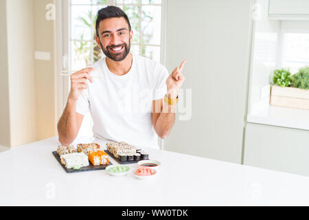 Stattliche Hispanic Mann essen asiatische Sushi mit Stäbchen sehr zufrieden zeigt mit Finger- und an der Seite Stockfoto