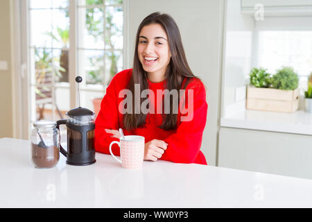 Junge schöne Frau, die Kaffee am Morgen lächelnd, Vorbereitung einer Tasse Latte für Frühstück Stockfoto