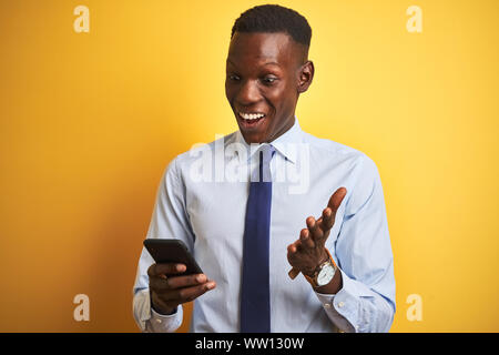 Afrikanische amerikanische Geschäftsmann mit Smartphone stehend über isolierte gelben Hintergrund sehr glücklich und aufgeregt, Sieger Ausdruck feiern Sieg s Stockfoto