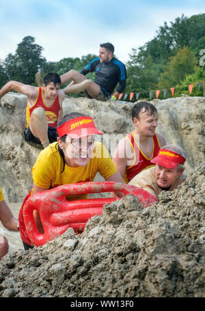 Ein Team von Konkurrenten gekleidet, wie Baywatch Rettungsschwimmer der 'Mud Meile verhandeln' an der haltbaren Mudder Ausdauer Event im Badminton Park, Gloucestershire U Stockfoto