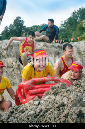 Ein Team von Konkurrenten gekleidet, wie Baywatch Rettungsschwimmer der 'Mud Meile verhandeln' an der haltbaren Mudder Ausdauer Event im Badminton Park, Gloucestershire U Stockfoto