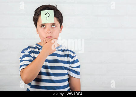 Kind denken mit Fragezeichen in Memo Post auf seiner Stirn über Ziegel Hintergrund Stockfoto