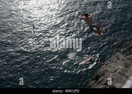 Ein Taucher springt von einer Klippe in Manarola, einer der fünf Fischerdörfer der Cinque Terre, die in der italienischen Riviera. Stockfoto