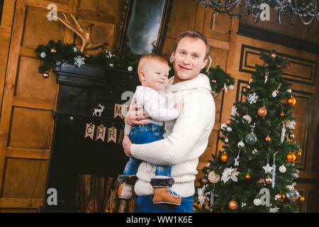 Mann und niedlichen Baby sind bereit, ins neue Jahr zu feiern. Gerne Vater und Kind Sohn in der Nähe von Weihnachtsbaum und Kamin in Weihnachten Abend. Thema Familie Stockfoto