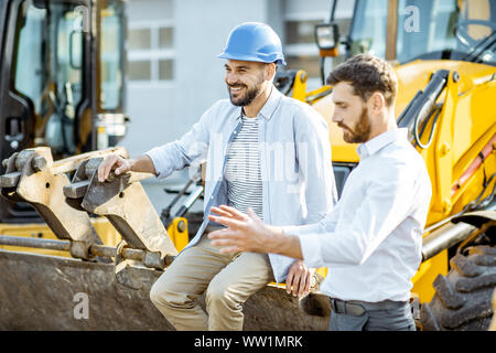 Builder Wahl schwere Maschinen für Bau, im Gespräch mit einem Verkaufsberater im Freigelände der einen Shop mit speziellen Fahrzeugen Stockfoto