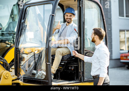 Builder Wahl schwere Maschinen für den Bau mit einem Verkaufsberater im Freigelände der einen Shop mit speziellen Fahrzeugen Stockfoto