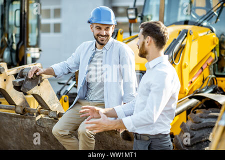 Builder Wahl schwere Maschinen für Bau, im Gespräch mit einem Verkaufsberater im Freigelände der einen Shop mit speziellen Fahrzeugen Stockfoto