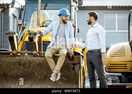 Builder Wahl schwere Maschinen für Bau, im Gespräch mit einem Verkaufsberater im Freigelände der einen Shop mit speziellen Fahrzeugen Stockfoto