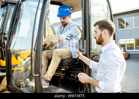 Builder Wahl schwere Maschinen für den Bau mit einem Verkaufsberater im Freigelände der einen Shop mit speziellen Fahrzeugen Stockfoto