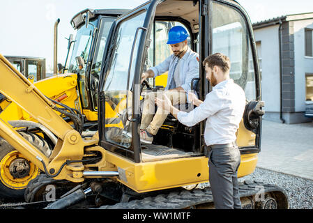 Builder Wahl schwere Maschinen für den Bau mit einem Verkaufsberater im Freigelände der einen Shop mit speziellen Fahrzeugen Stockfoto