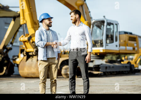 Builder Wahl schwere Maschinen für Bau, im Gespräch mit einem Verkaufsberater im Freigelände der einen Shop mit speziellen Fahrzeugen Stockfoto