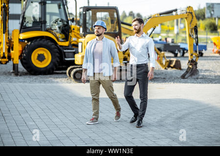 Builder Wahl schwere Maschinen für Bau, im Gespräch mit einem Verkaufsberater im Freigelände der einen Shop mit speziellen Fahrzeugen Stockfoto