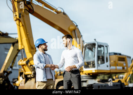 Builder Wahl schwere Maschinen für Bau, im Gespräch mit einem Verkaufsberater im Freigelände der einen Shop mit speziellen Fahrzeugen Stockfoto