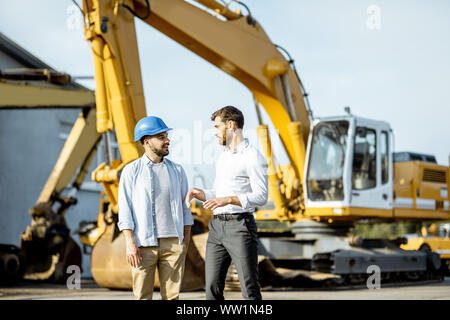 Builder Wahl schwere Maschinen für Bau, im Gespräch mit einem Verkaufsberater im Freigelände der einen Shop mit speziellen Fahrzeugen Stockfoto