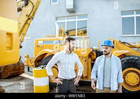 Builder Wahl schwere Maschinen für Bau, im Gespräch mit einem Verkaufsberater im Freigelände der einen Shop mit speziellen Fahrzeugen Stockfoto