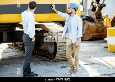 Builder Wahl schwere Maschinen für Bau, im Gespräch mit einem Verkaufsberater im Freigelände der einen Shop mit speziellen Fahrzeugen Stockfoto