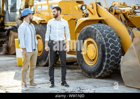 Builder Wahl schwere Maschinen für Bau, im Gespräch mit einem Verkaufsberater im Freigelände der einen Shop mit speziellen Fahrzeugen Stockfoto