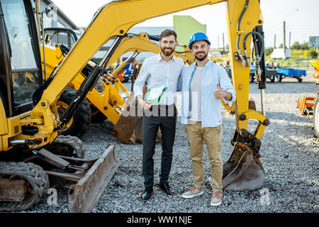 Builder Wahl schwere Maschinen für Bau, im Gespräch mit einem Verkaufsberater im Freigelände der einen Shop mit speziellen Fahrzeugen Stockfoto