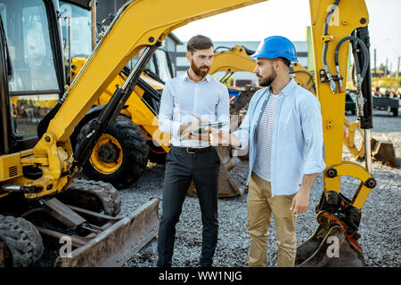 Builder Wahl schwere Maschinen für Bau, im Gespräch mit einem Verkaufsberater im Freigelände der einen Shop mit speziellen Fahrzeugen Stockfoto
