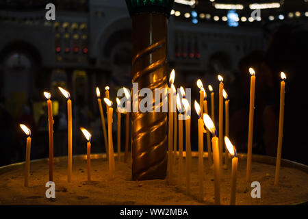 Wachs Kerzen anzünden auf dem Altar in der Kirche in den Tempel Gottes vor dem Hintergrund der betenden Gläubigen Stockfoto