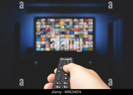 Multimedia Video Konzept auf TV im dunklen Zimmer setzen. Man Fernsehen mit Fernbedienung in der Hand. Stockfoto