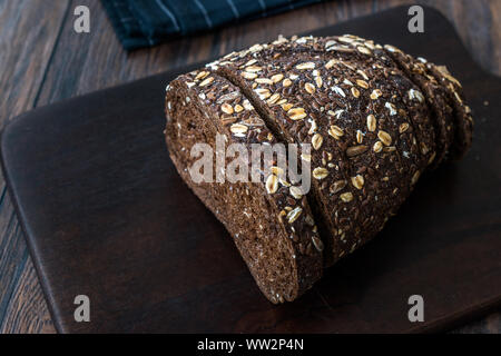 Malz Brotscheiben mit Hafer und Leinsamen auf dunklen Holz- Board. Bio Bäckerei Essen. Stockfoto