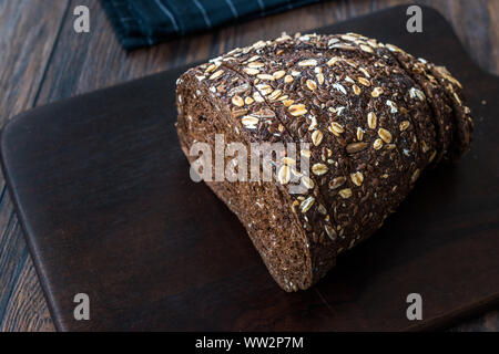 Malz Brotscheiben mit Hafer und Leinsamen auf dunklen Holz- Board. Bio Bäckerei Essen. Stockfoto