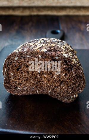 Malz Brotscheiben mit Hafer und Leinsamen auf dunklen Holz- Board. Bio Bäckerei Essen. Stockfoto