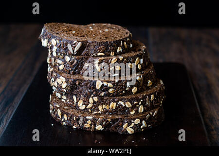 Malz Brotscheiben mit Hafer und Leinsamen auf dunklen Holz- Board. Bio Bäckerei Essen. Stockfoto