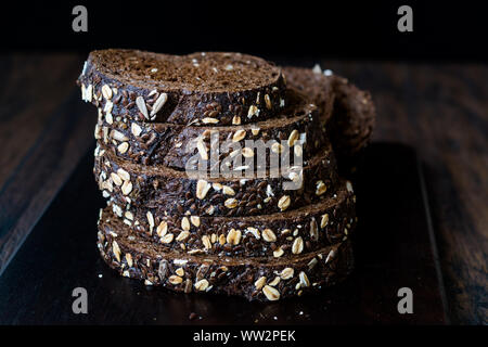 Malz Brotscheiben mit Hafer und Leinsamen auf dunklen Holz- Board. Bio Bäckerei Essen. Stockfoto