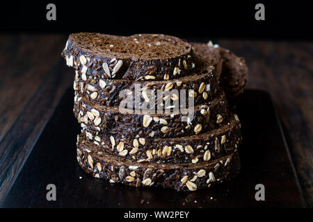 Malz Brotscheiben mit Hafer und Leinsamen auf dunklen Holz- Board. Bio Bäckerei Essen. Stockfoto