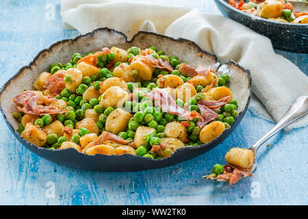 Gnocchi mit grünen Erbsen, Pesto, Schinken und Chorizo in eine Schüssel geben. Stockfoto