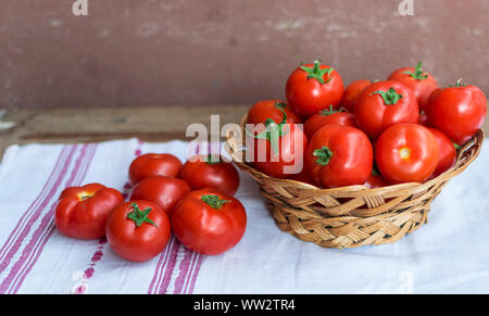 Frische rote Tomaten in Korb auf Holztisch mit Tuch mit Ethno Motive. Stockfoto