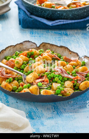 Gnocchi mit grünen Erbsen, Pesto, Schinken und Chorizo in eine Schüssel geben. Stockfoto