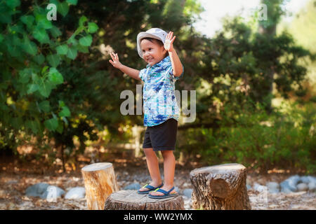 Ein Lächeln 3 Jahre alten Jungen in einer freien, stand auf einem hölzernen, mit den Armen ausgestreckt, Balance. Stockfoto