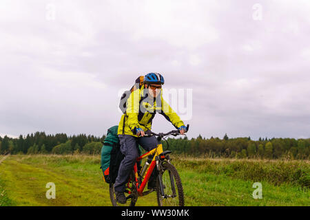 Männliche bikepacker reitet auf einem Feldweg durch ein Feld an einem bewölkten Herbst Tag Stockfoto