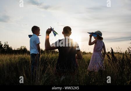 Vater spielen Flugzeuge mit Sohn und Tochter auf einer Wiese bei Sonnenuntergang Stockfoto