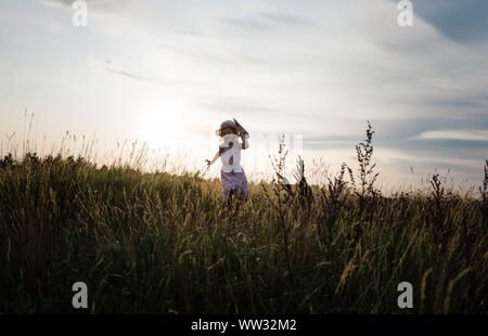 Mädchen läuft durch eine Wiese mit einem Papierflieger bei Sonnenuntergang Stockfoto