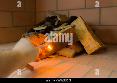 Eine Hand mit einem brennenden Streichholz Feuer zu geben einige Protokolle. Stockfoto