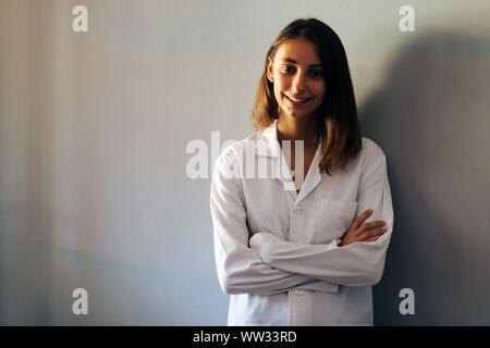 Junge weibliche Arzt lächelnd und mit verschränkten Armen auf einem grauen Hintergrund. Medizin Konzept. Stockfoto