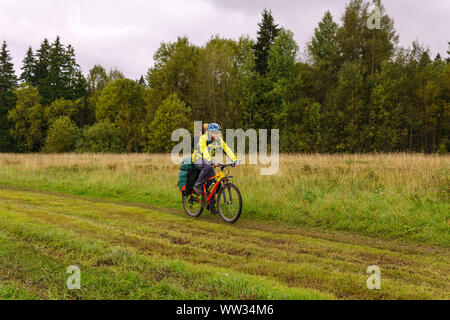 Männliche radfahren Tourist auf einer Schotterstraße durch ein Feld an einem bewölkten Herbst Tag Stockfoto