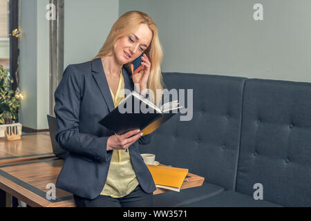 Junge Geschäftsfrau spricht auf dem Smartphone halten Sie das Notebook im Büro. Geschäftskonzept. Stockfoto